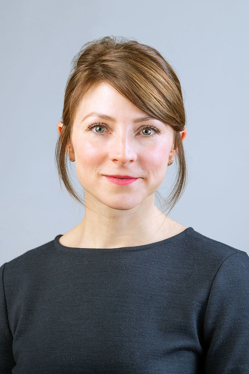 Anne Brancky wearing a black shirt against a light gray background.