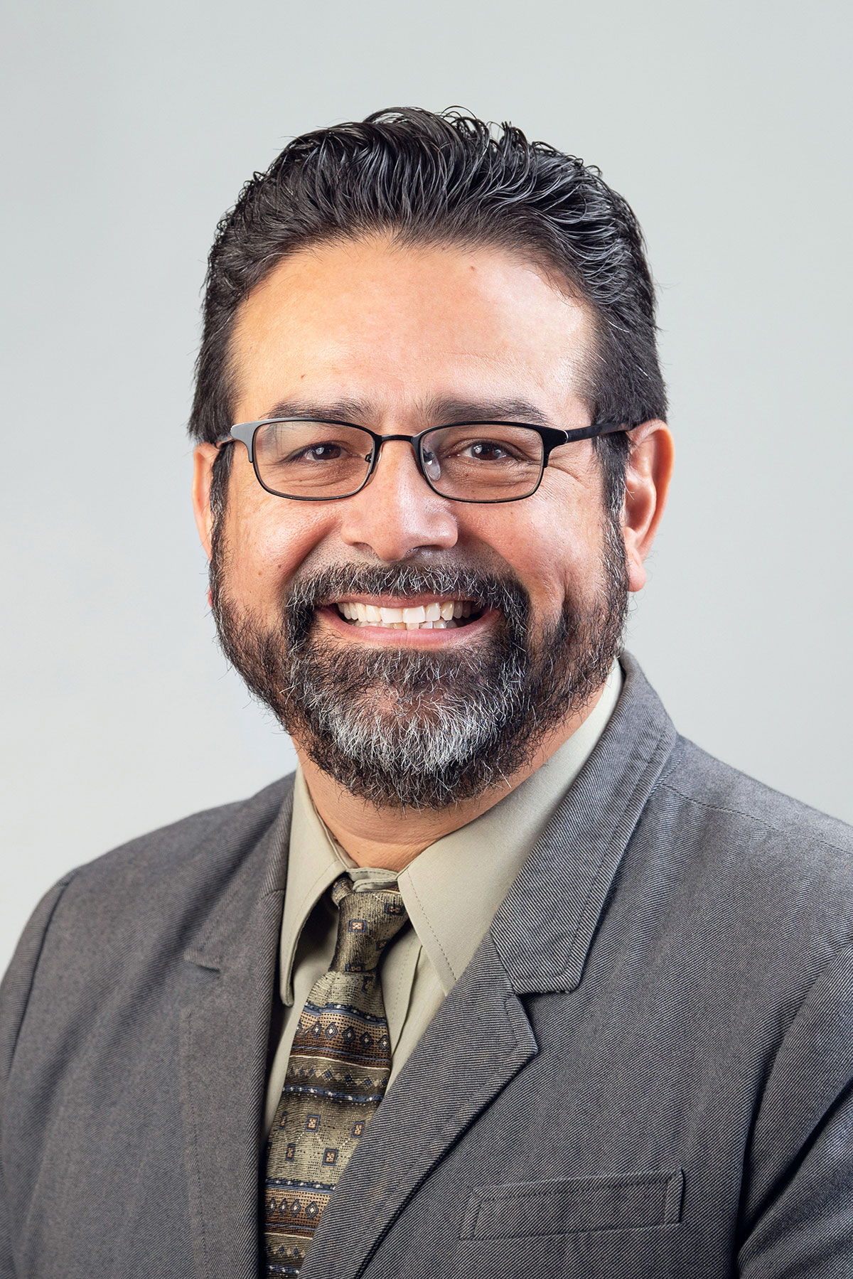 Jaime Liborio Del Razo wearing a light colored shirt, dark gray jacket against a gray background.