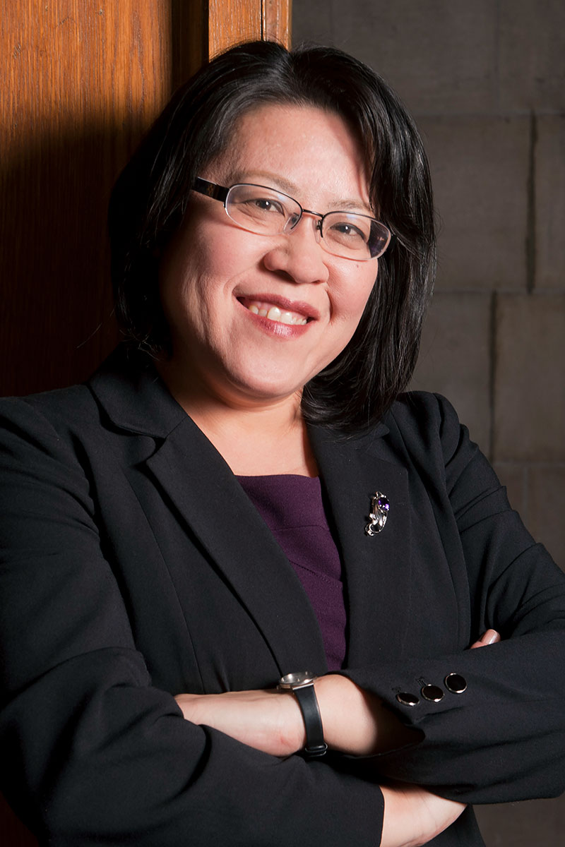 Hiromi Tsuchiya Dollase wearing a purple shirt and black jacket with arms folded. 