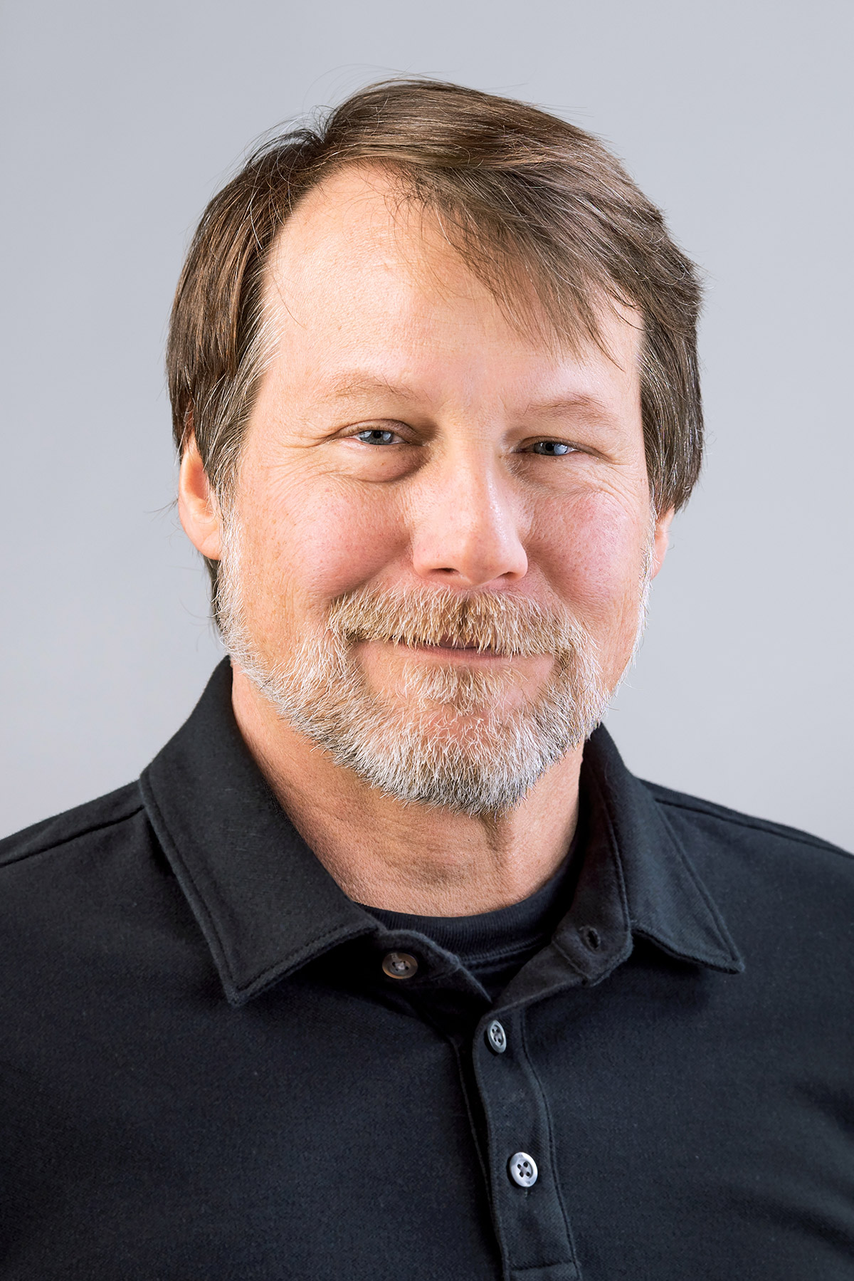 William Hoynes wearing a black collared shirt with a gray background.