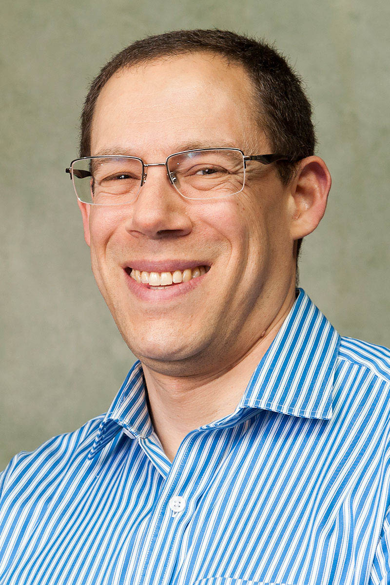 Jeffrey S. Seidman wearing a blue and white striped collared shirt against a light background.