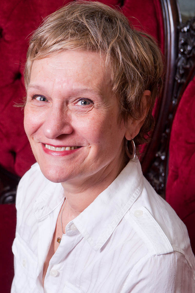 Patricia-Pia Célérier wearing a white shirt sitting in a red velvet chair.