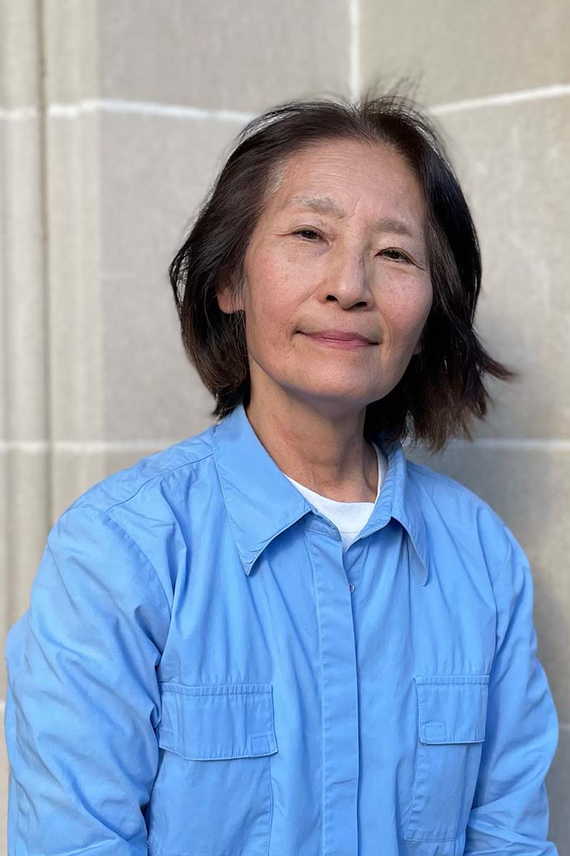 A person with shoulder-length black hair and a blue shirt looks at the viewer.