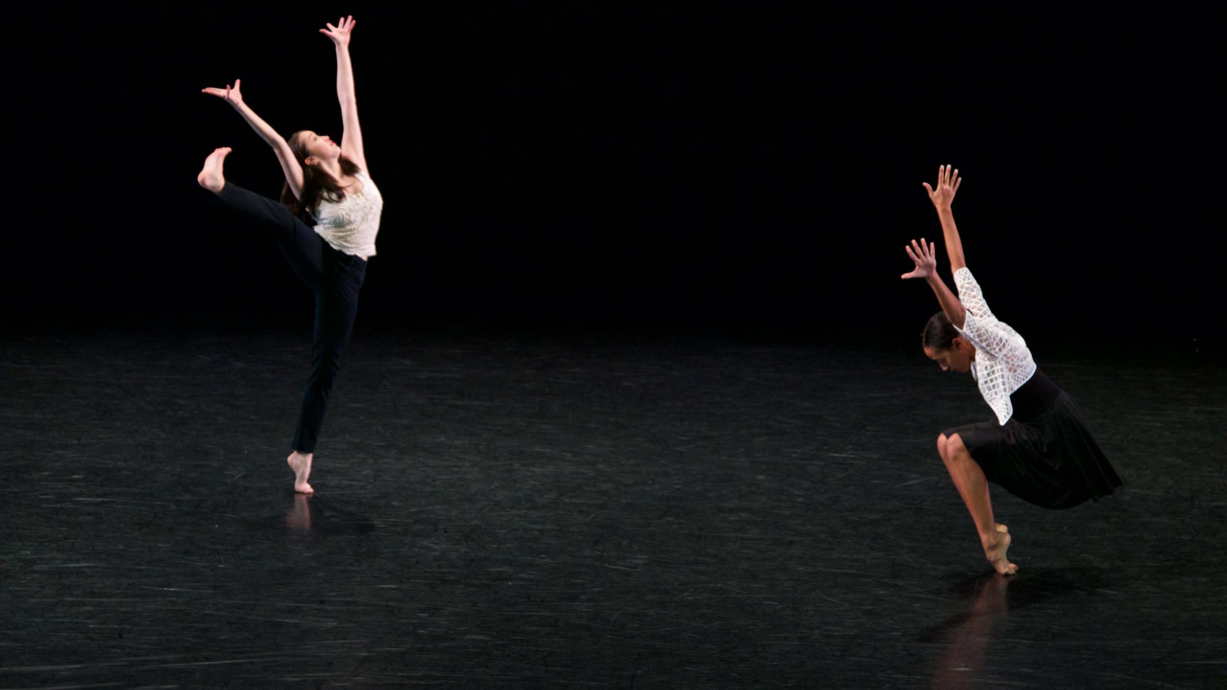 Two dancers pose on a darkened stage. Photo by Mitchell Davis ’19.