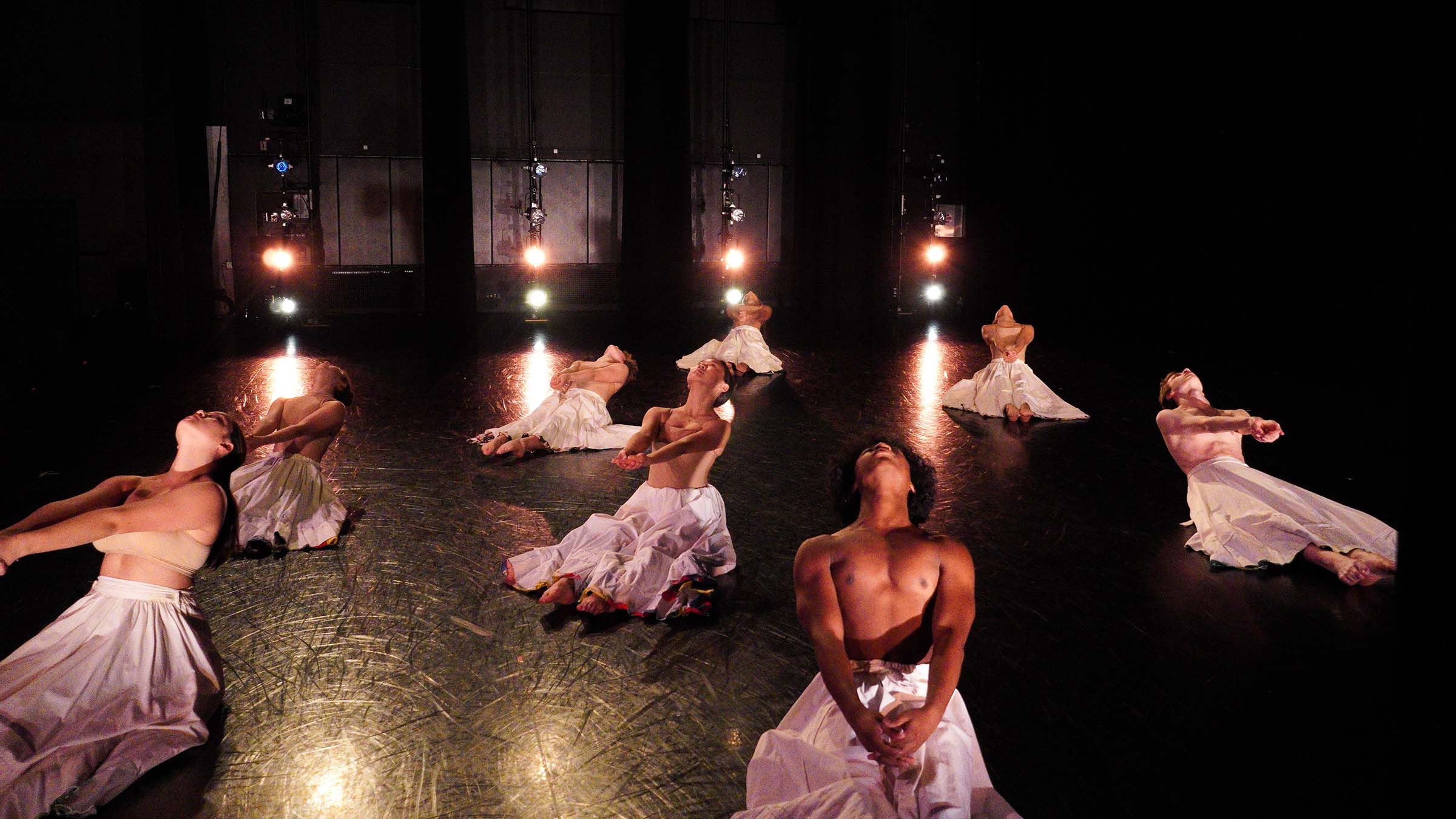 A group of dancers poses on a mostly dark stage, lit by blazing lights in the background. Photo by Yesmina Townsley ’23.