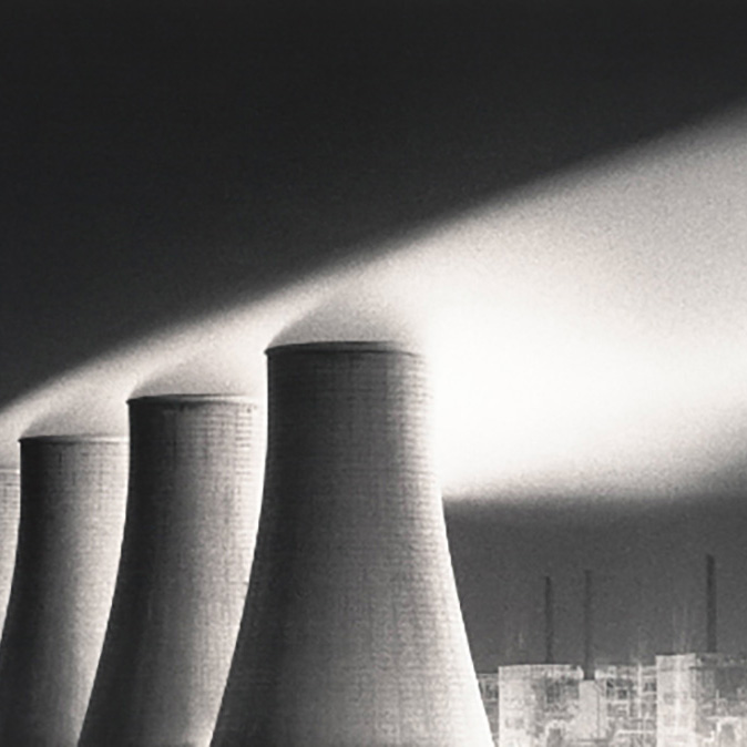A monochrome print of four tall conical towers of a nuclear power station with steam coming out of them.