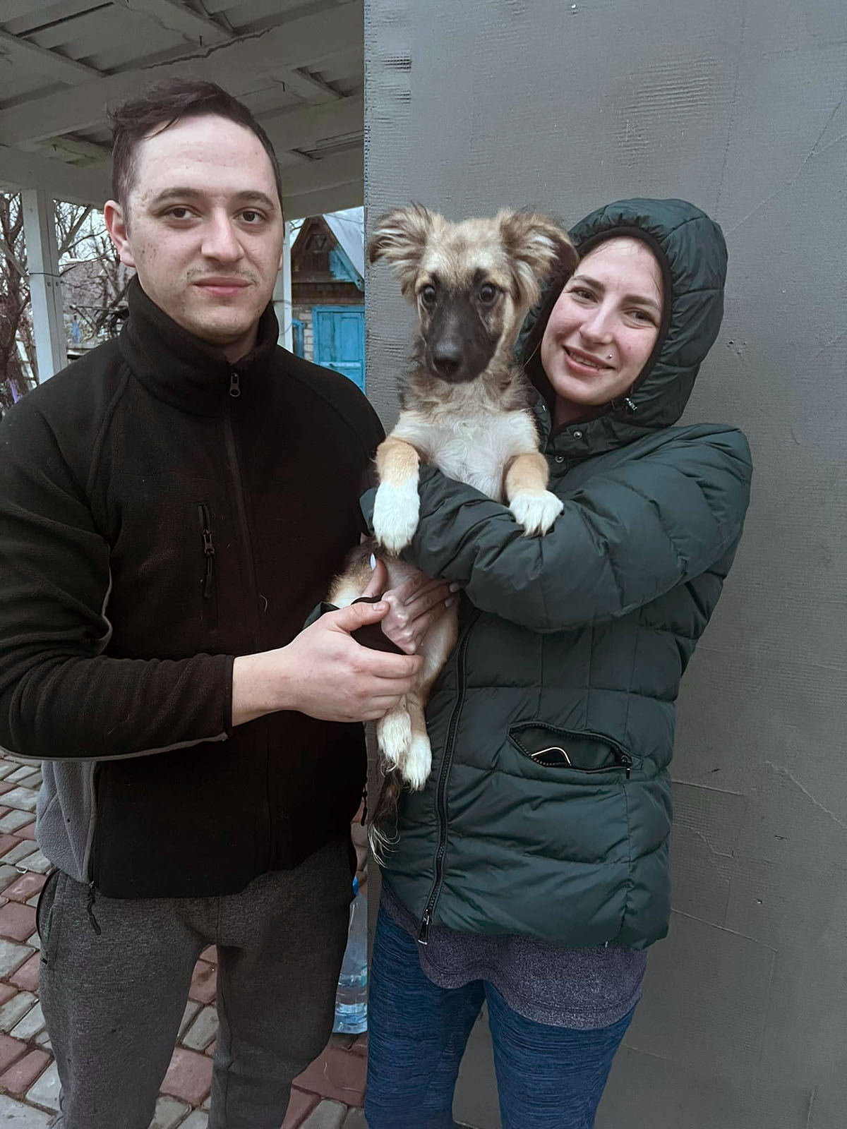 Two people from the Ray of Hope shelter holding a growing puppy.