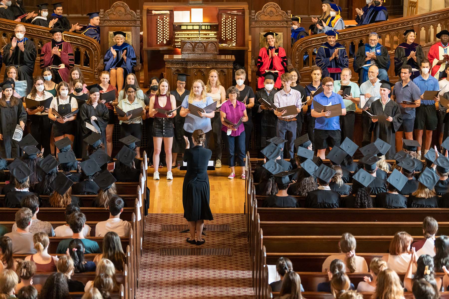 A choir of students performs in front of the assembled graduates.