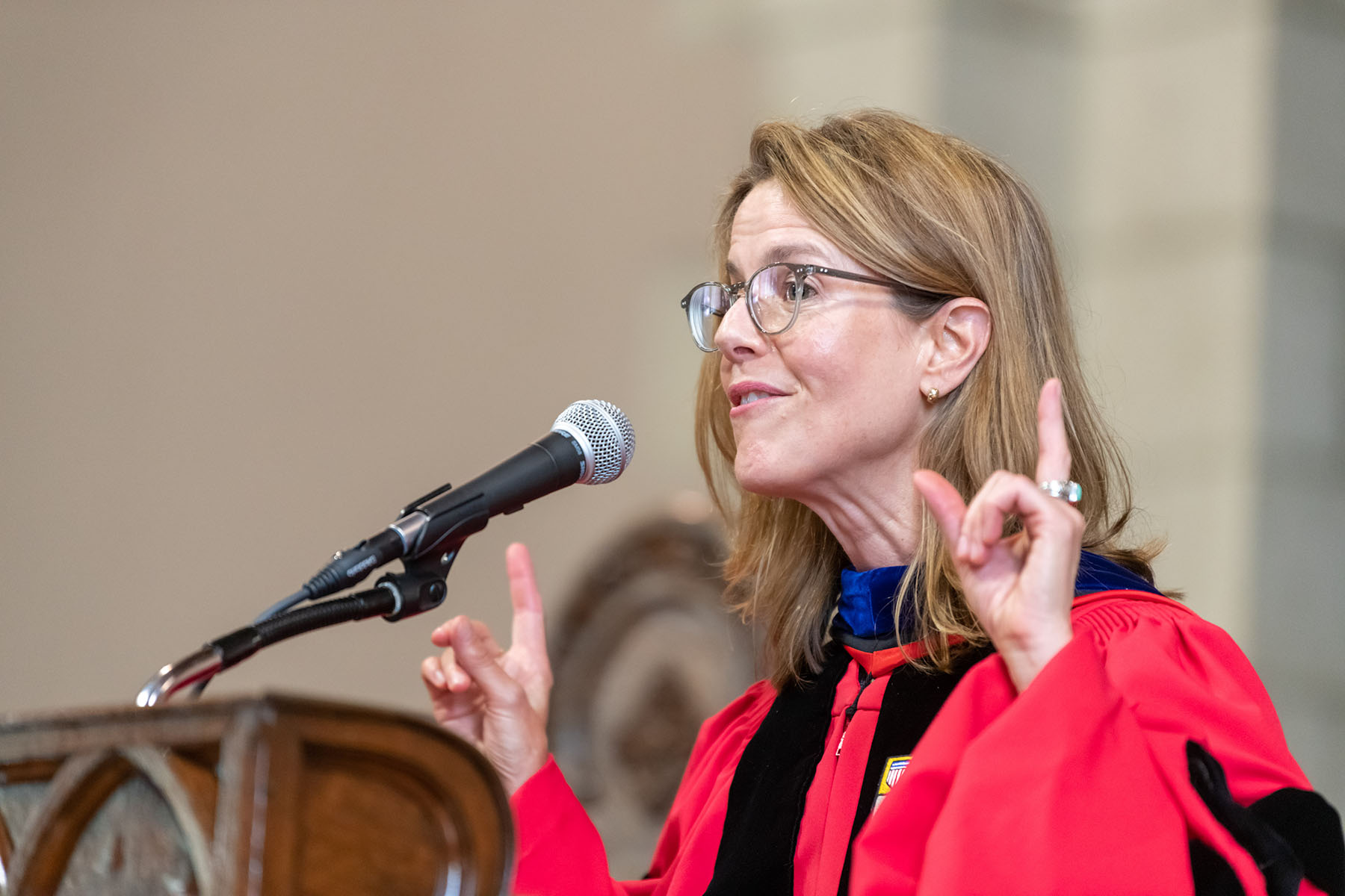 Nancy Bisaha, Professor of History, speaks in front of a podium. Bisaha wears a red robe and no cap.