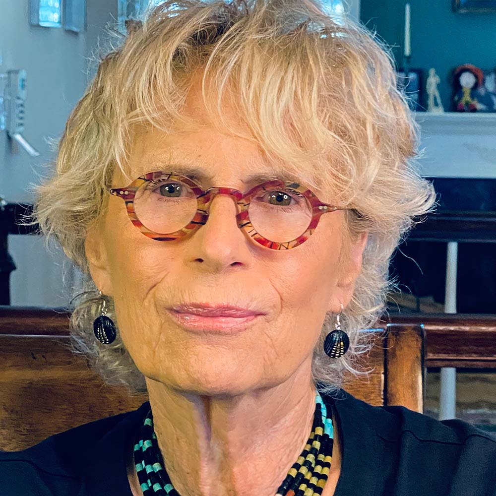 Head and shoulder photo of Brenda Feigen wearing navy shirt and multi colored necklace