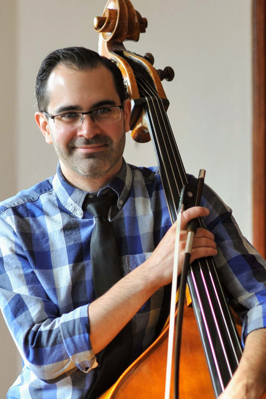 Daniel Merriman, wearing a blue checkered collared shirt holding a double bass. 