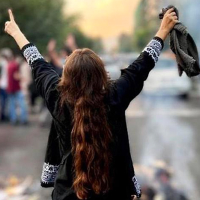 a woman at a protest, viewed from the back with her arms in the air.