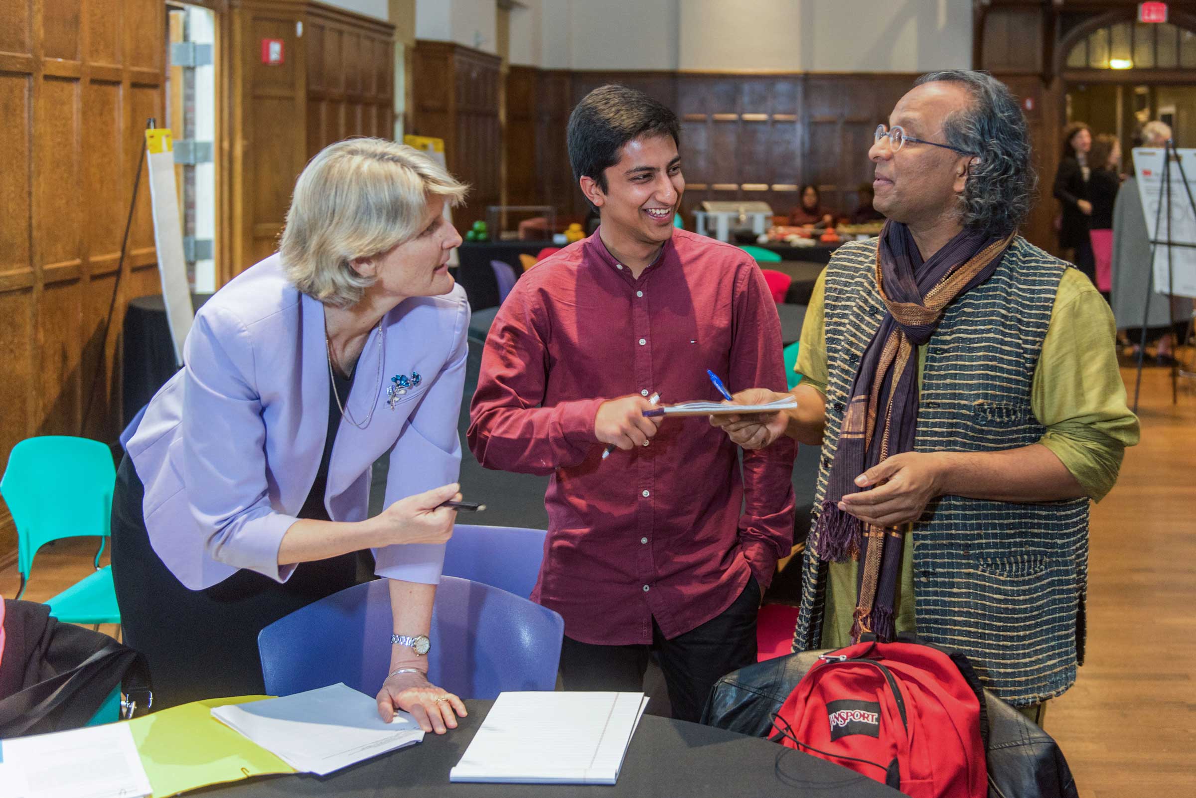 three standing people behind a table talking animatedly and writing things down on pads