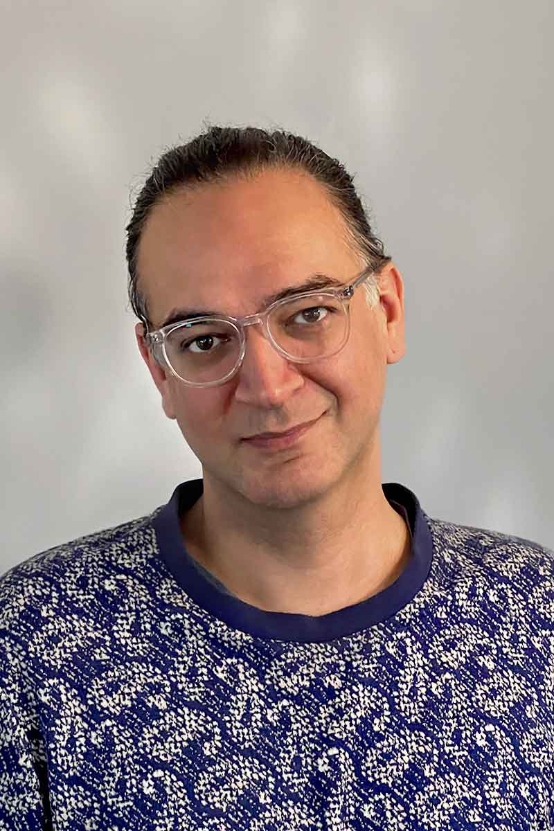 A portrait of a person with dark hair and glasses looking at the camera.