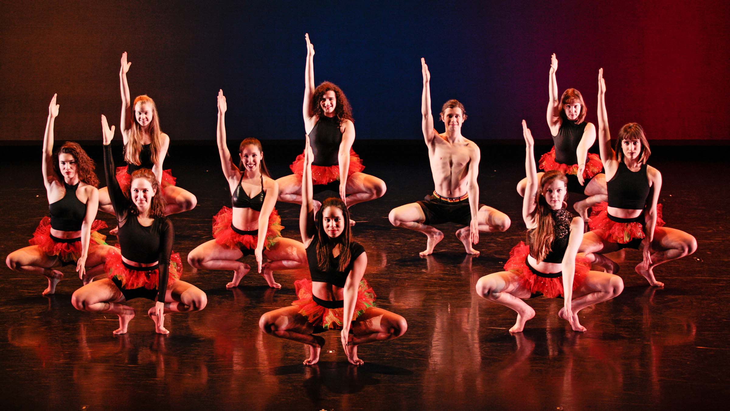 Vassar Repertory Dance Theatre dancers on stage wearing red and black, squatting with right arm up