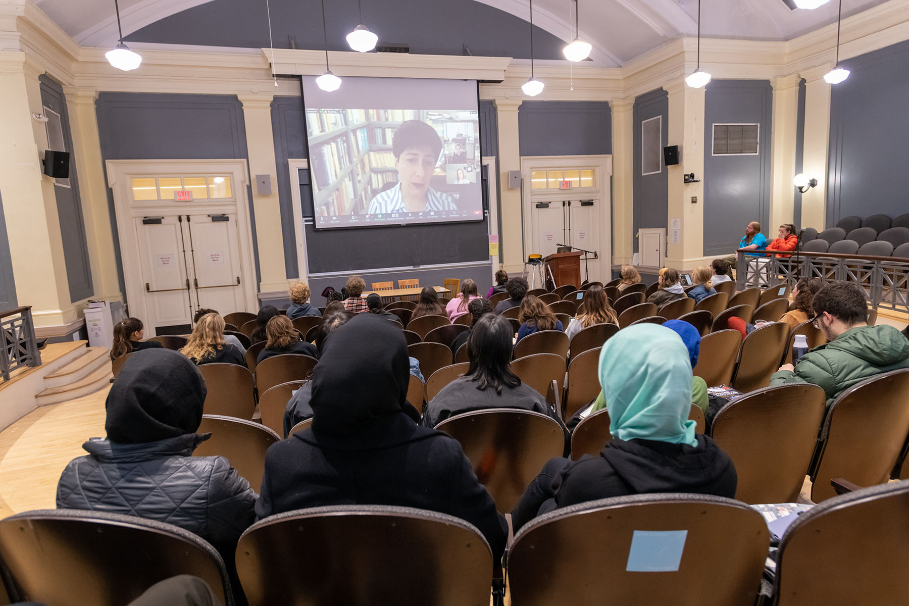 Fatemeh Sadeghi speaking via Zoom on a screen in an auditorium full of people