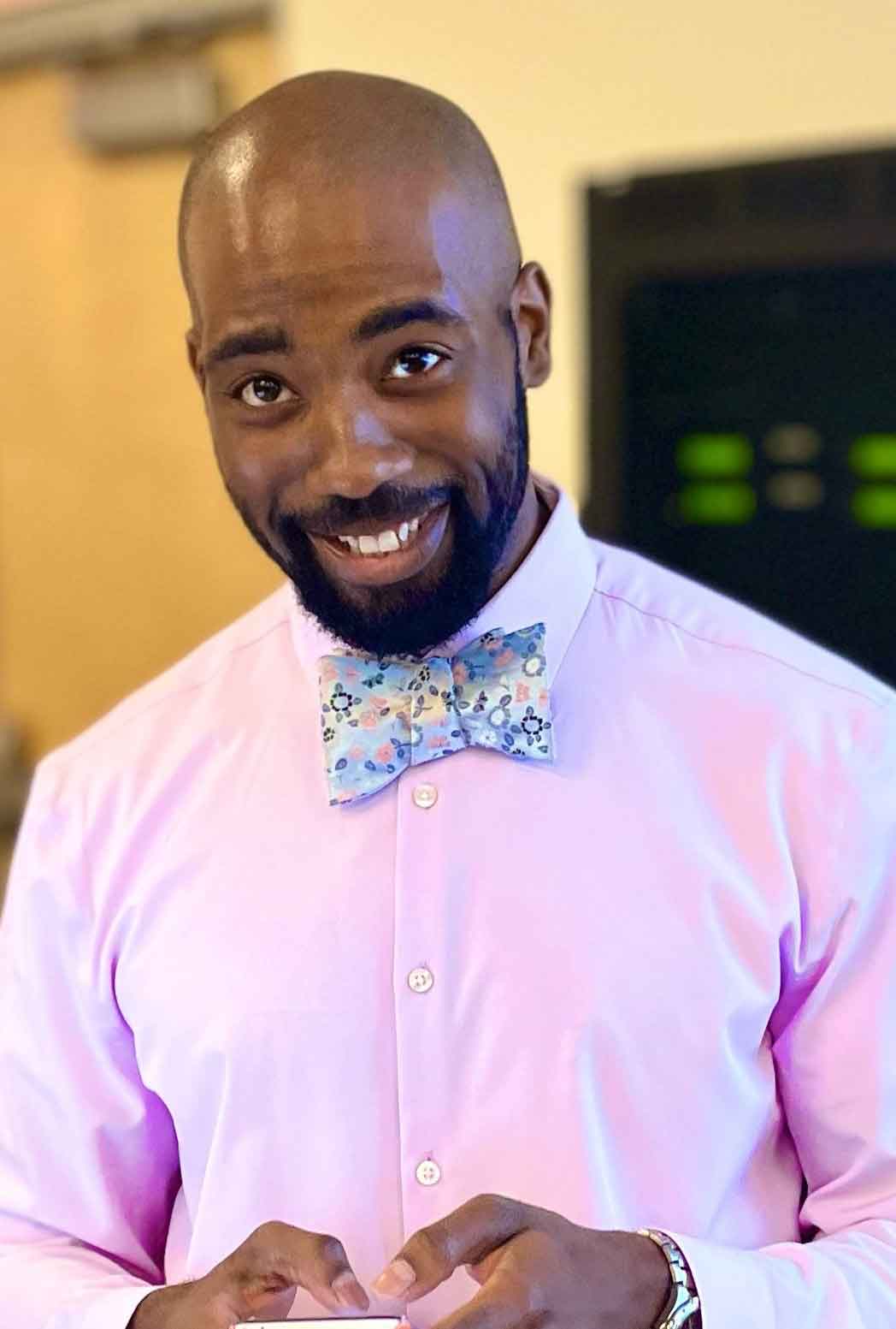 A portrait of a person wearing a pink shirt and bowtie looking at the camera.