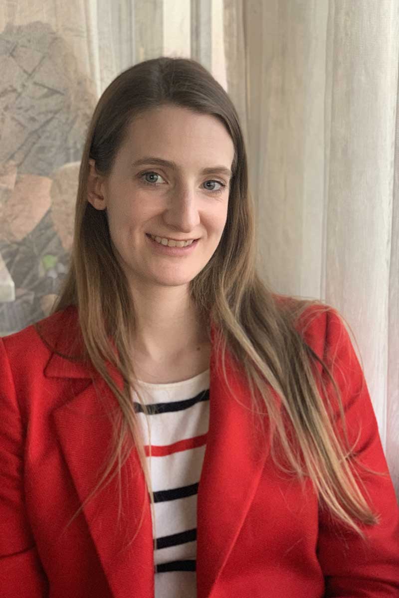 A person with long hair and a red coat smiles at the camera.