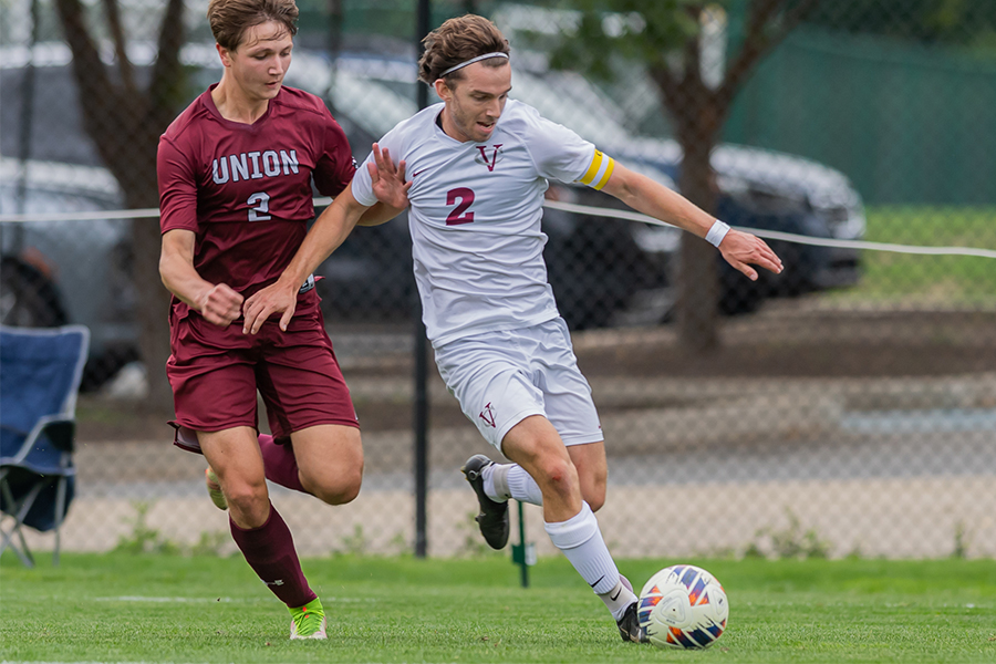 Owen Fauth kicks the ball while being closely guarded from behind by an opposing player.
