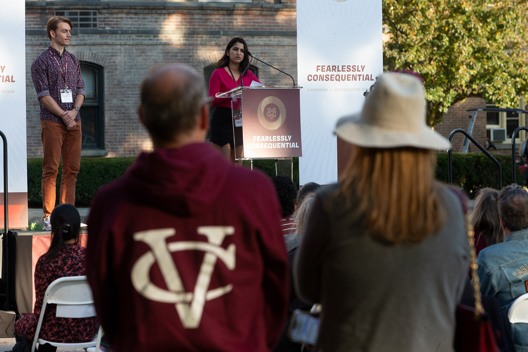 A woman speaking at a podium outside from front of an audience