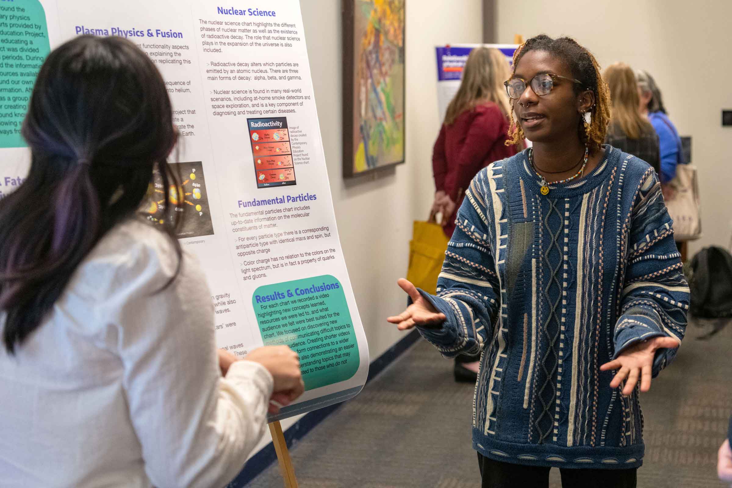 Student standing in front of a poster explaining it while gesticulating to another person