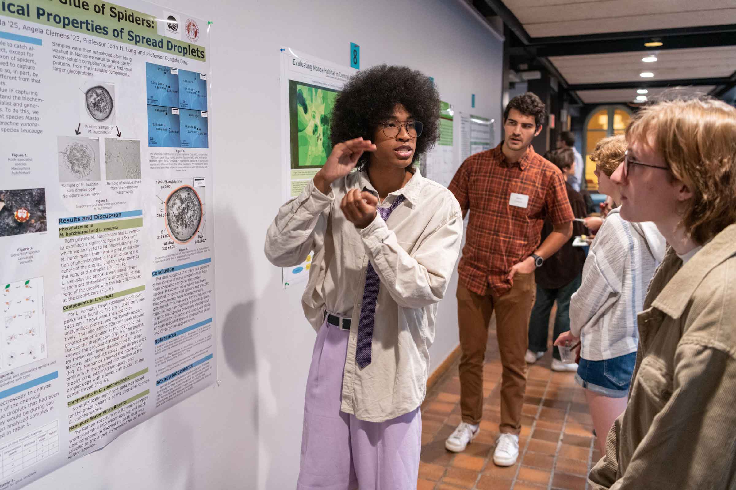 Student standing in front of a poster explaining it while gesticulating to a group of people