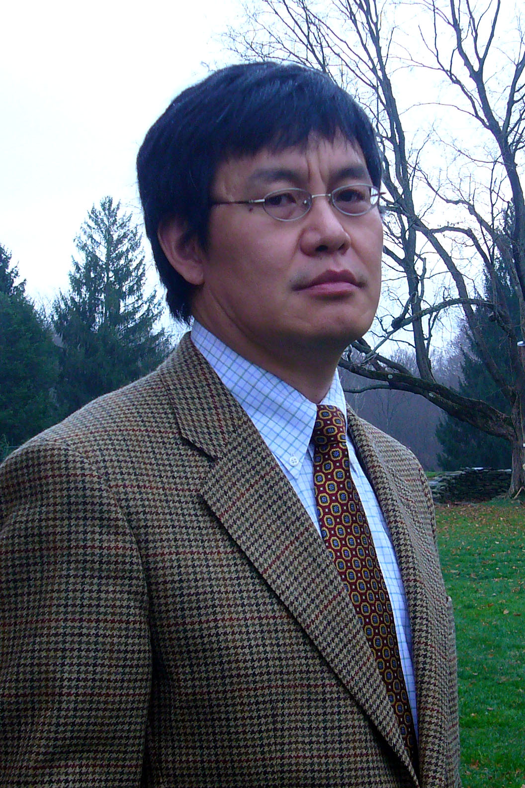 Pictured: Haoming Liu - Man with a suit and glasses standing outside with grass and trees in the background.