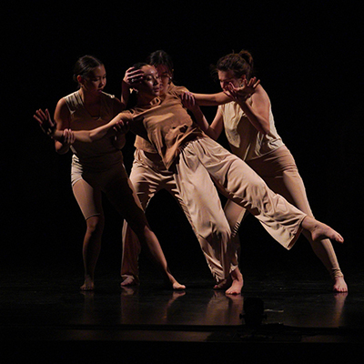 Three dancers onstage support a fourth dancer who is leaning back.