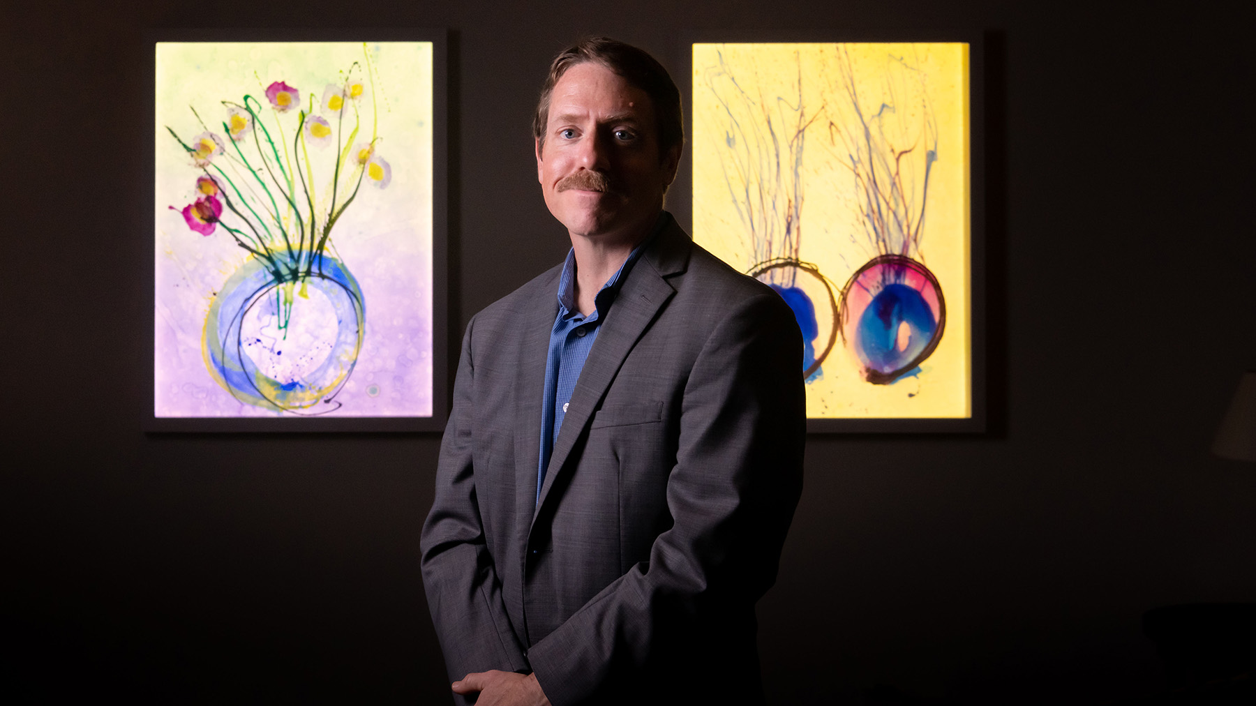 Library Director Andrew Ashton standing in front of the “Glass on Glass” works installed in the library 