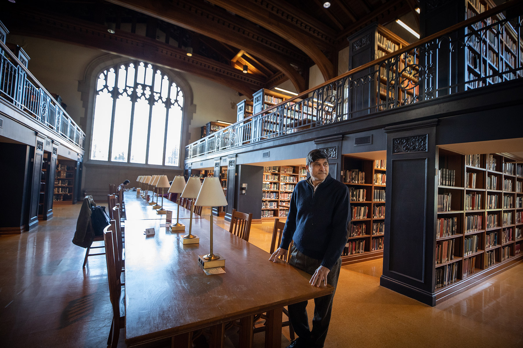 Ronald Patkus standing at a table in the Vassar Library with book shelves behind him.