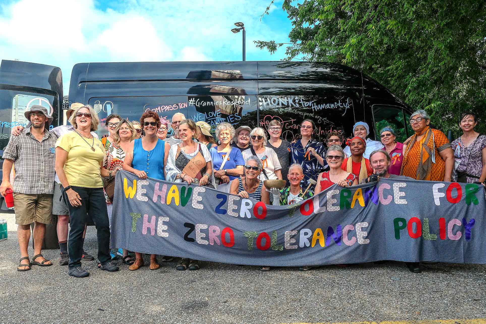Large group shot of people in front of a bus holding a banner that reads: We have zero tolerance for the zero tolerance policy