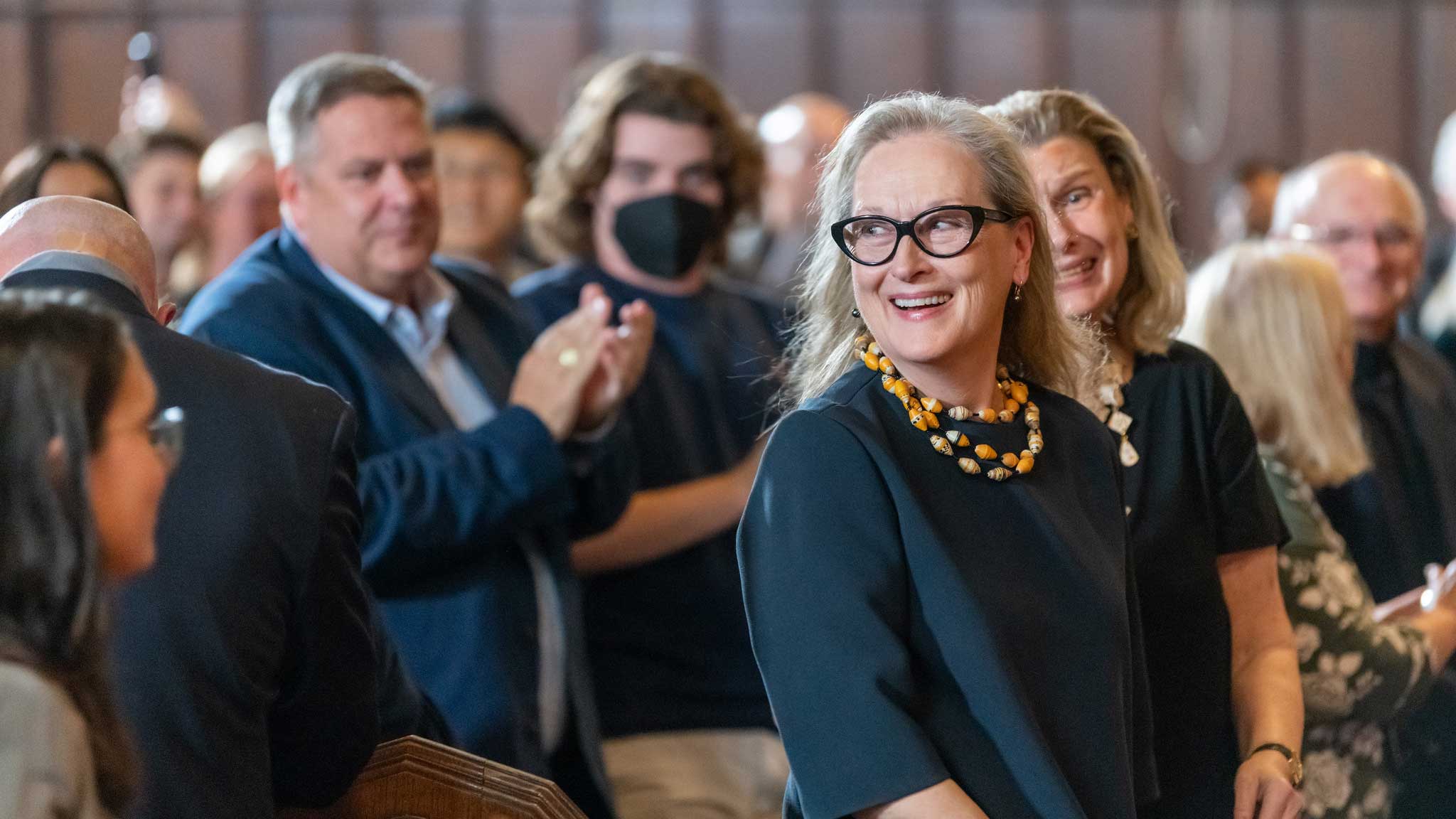 Meryl Streep standing in an audience while smiling and looking back