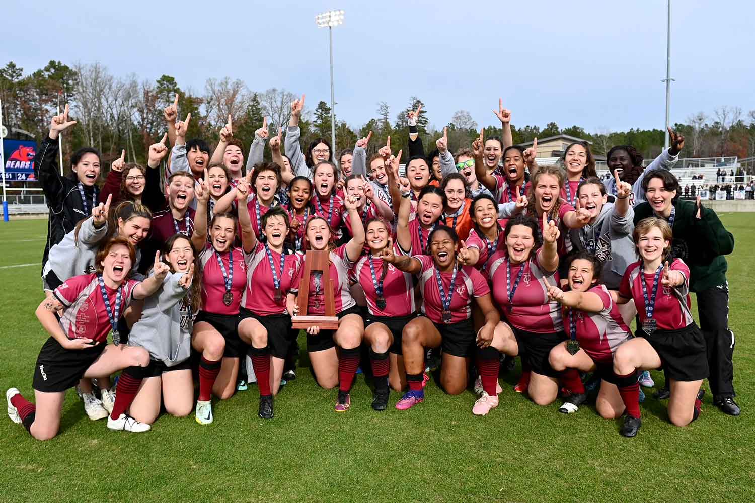 Group shot of Vassar women's rugby team on the field holding up hands making the number one sign