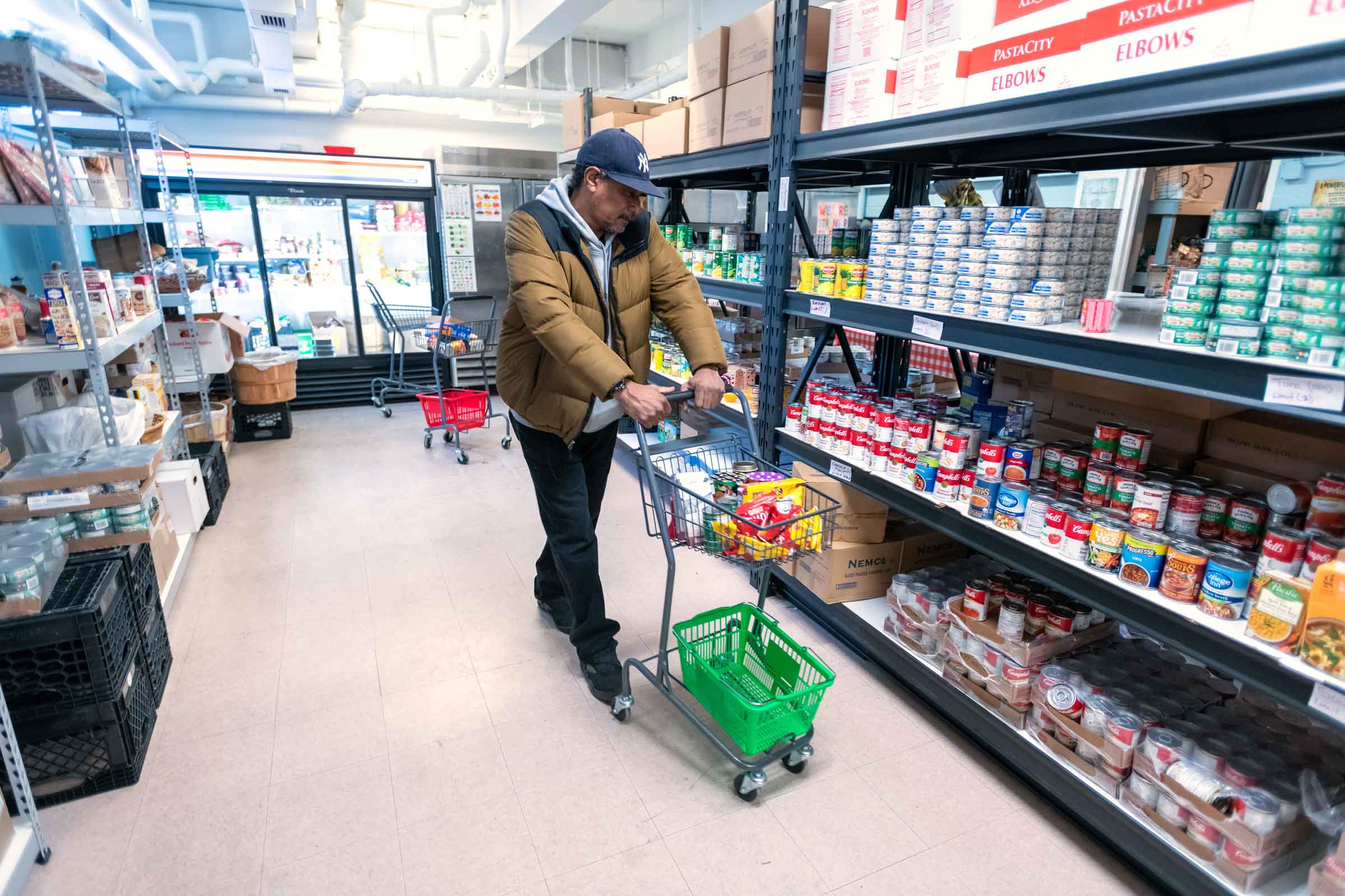 Person pushing a shopping cart down an isle with shelves of canned food 