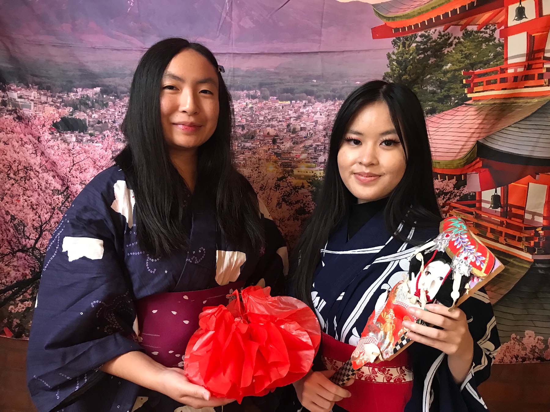 Two people in traditional Asian clothing in front of a banner of Mt. Fuji and a Japanese temple in the background