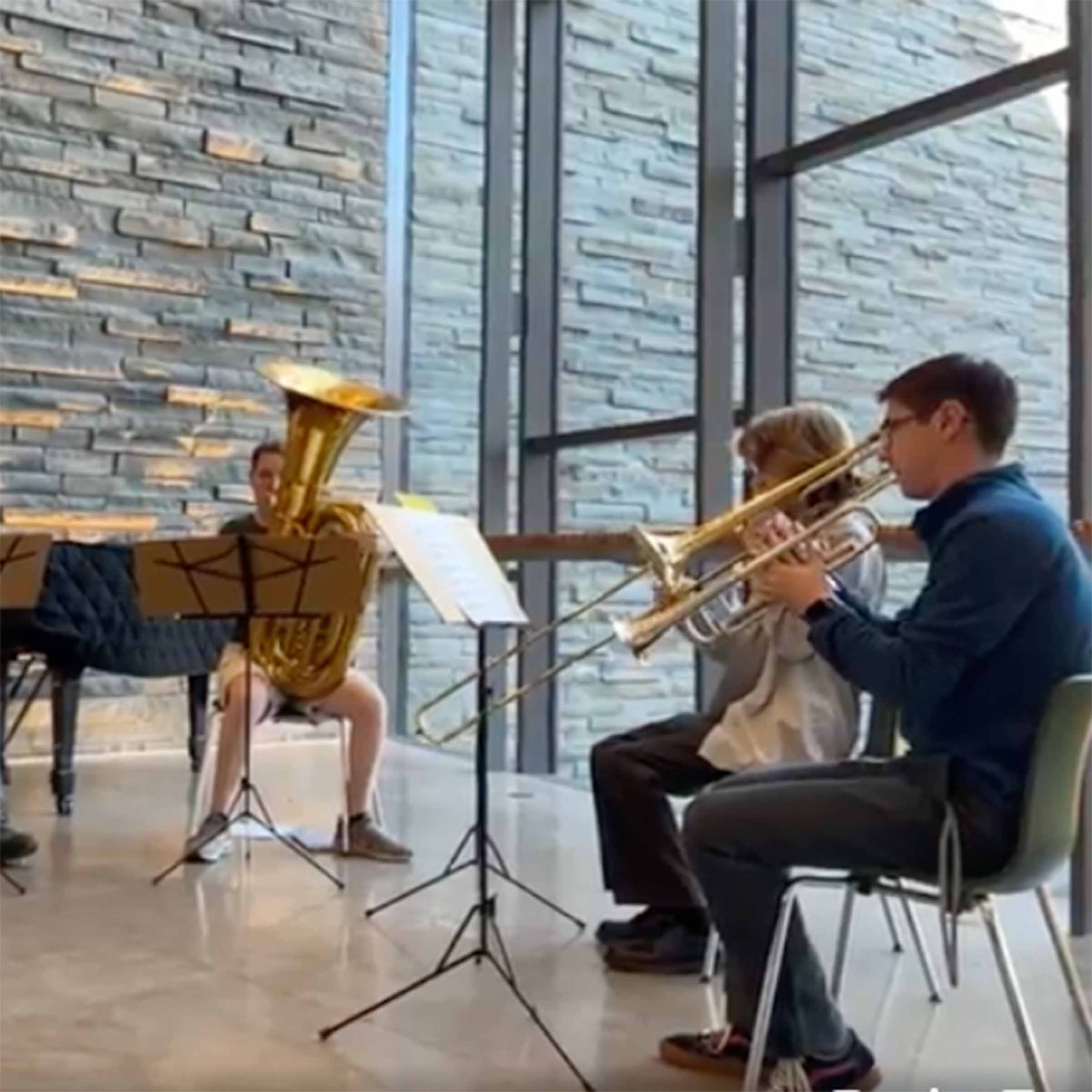 Three musicians playing tuba, trombone and trumpet in a large space