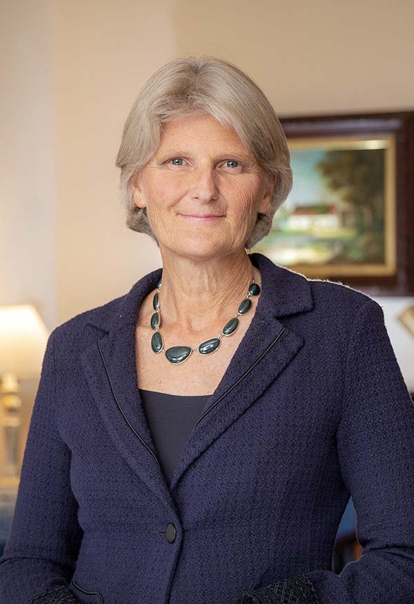 A person with mid-length gray hair and a dark blue jacket smiles at the camera