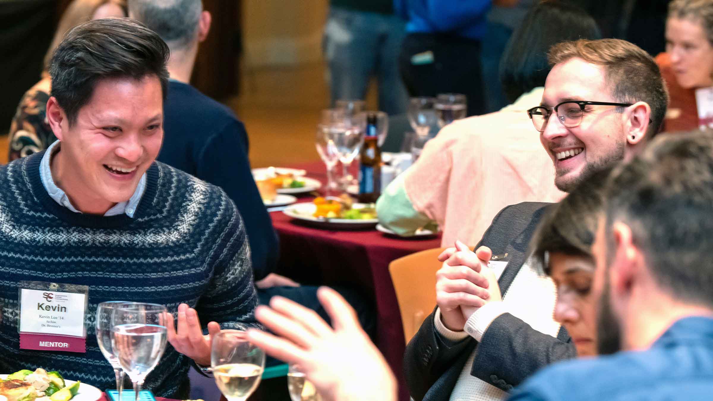 Four people seated at a table with food and drink laughing and smiling