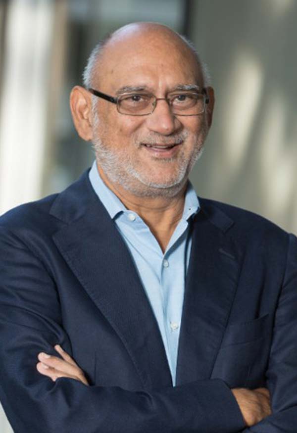 A person with a bald head, glasses, and facial hair smiles at the camera. The person is wearing a dark suit.