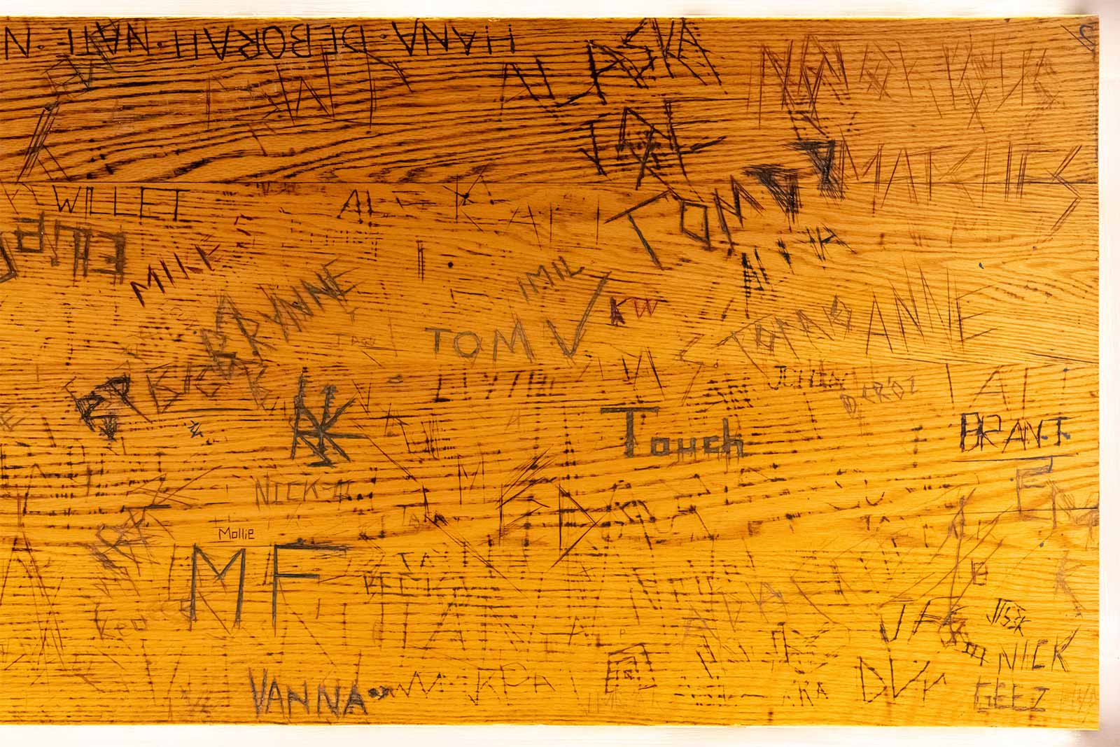 A photo of a wooden surface with names and letters roughly scratched into it