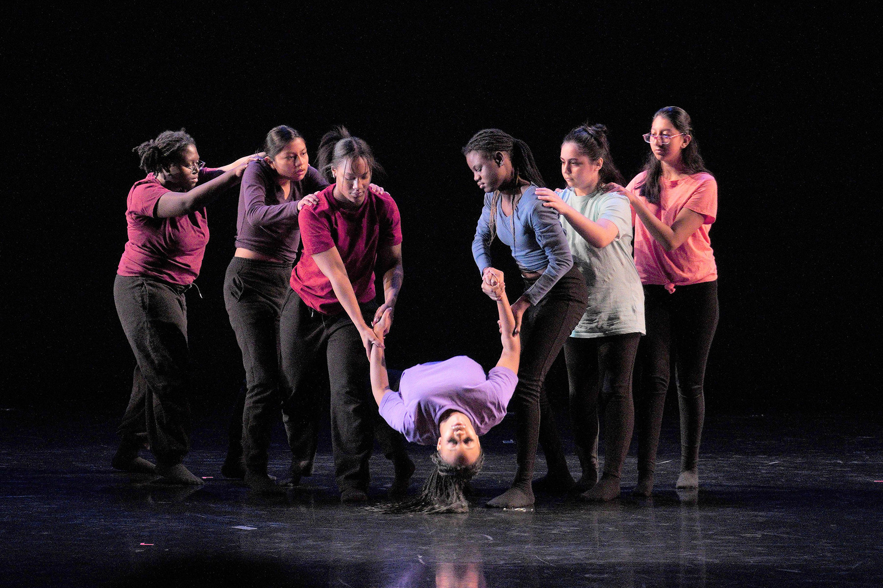 Seven women on a stage holding one of them in a dance position