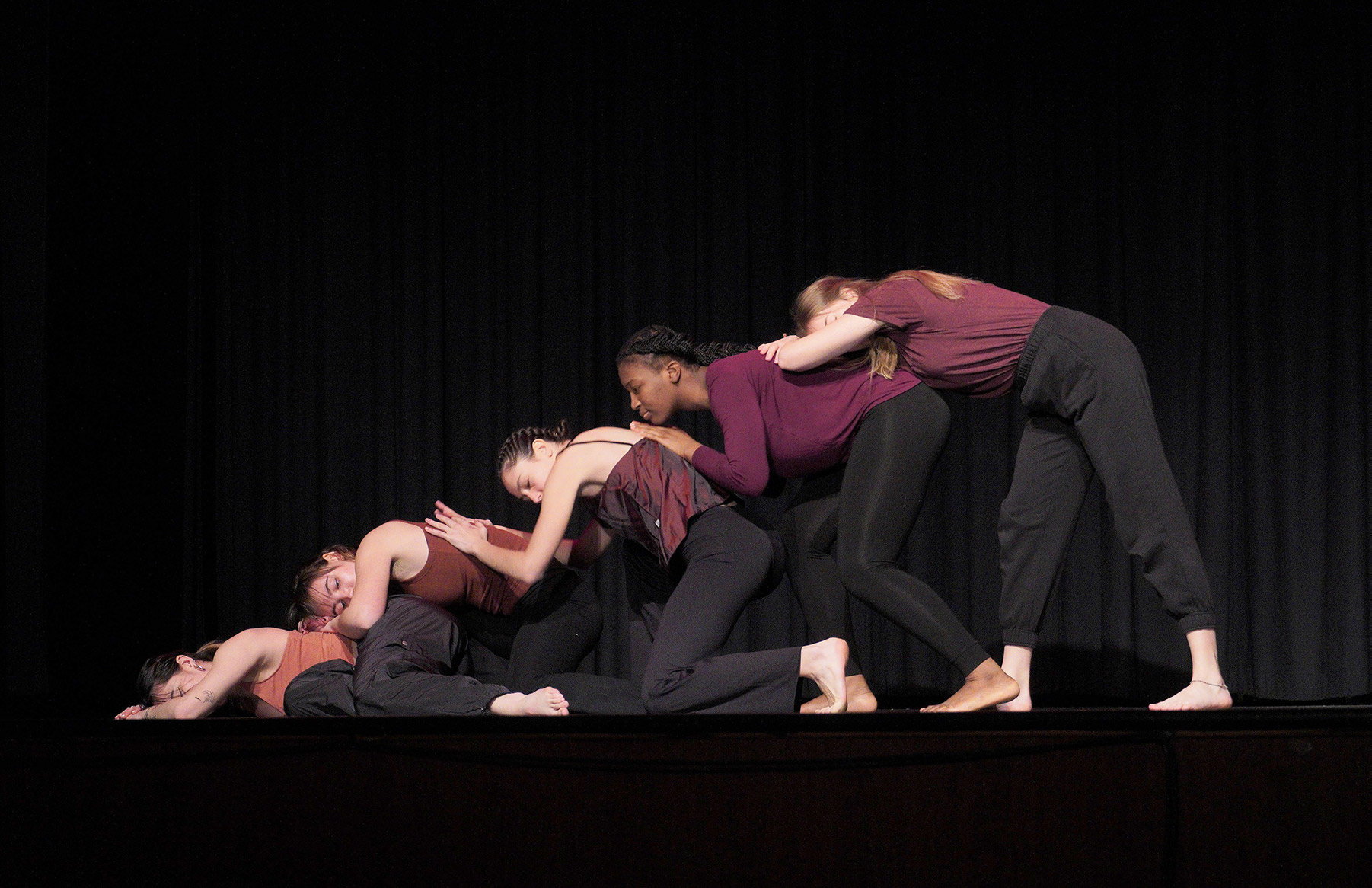 Five women on a stage leaning on each other's backs in a line