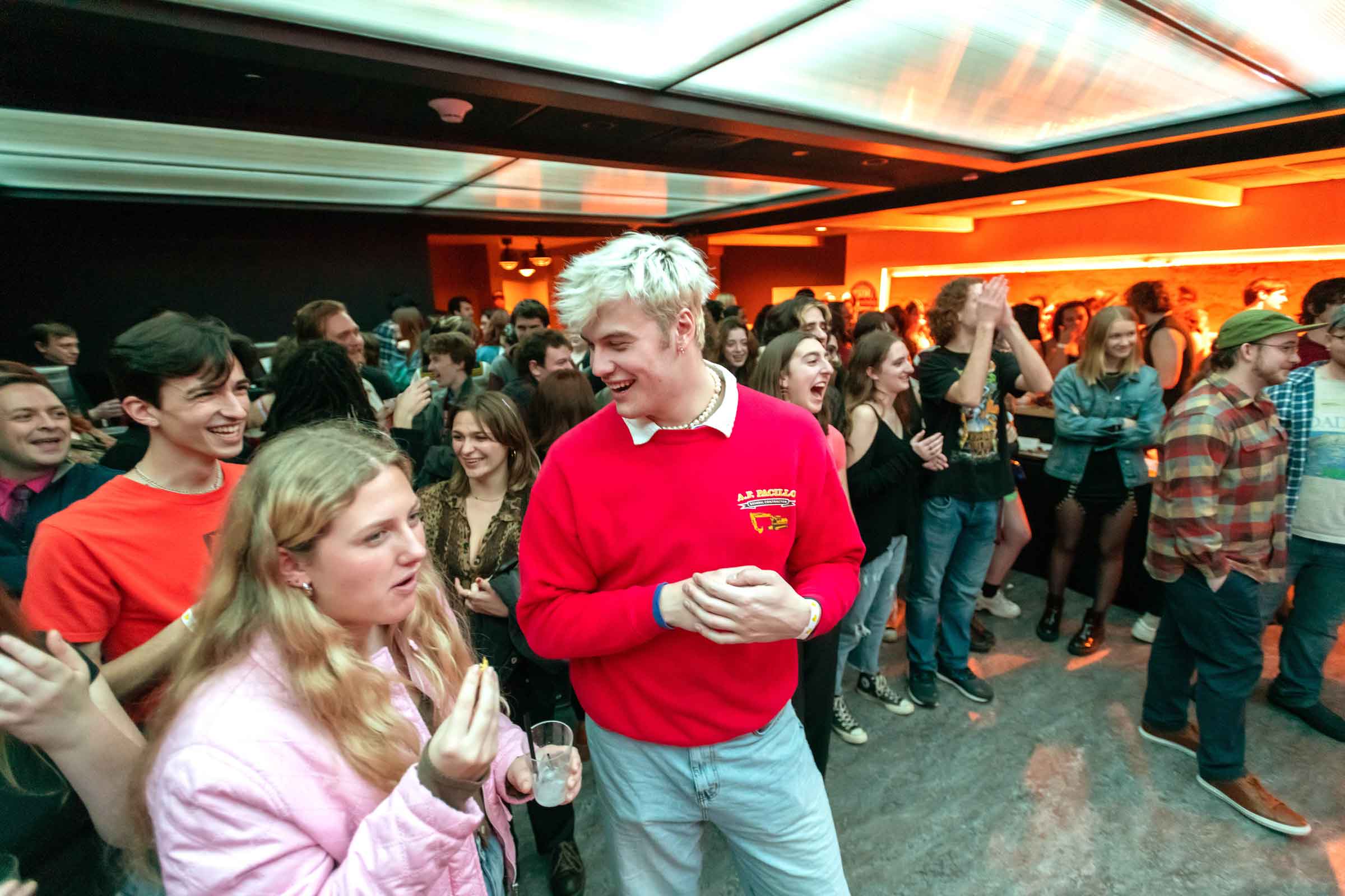 A crowd of people in a club setting smiling and talking with the main event offstage