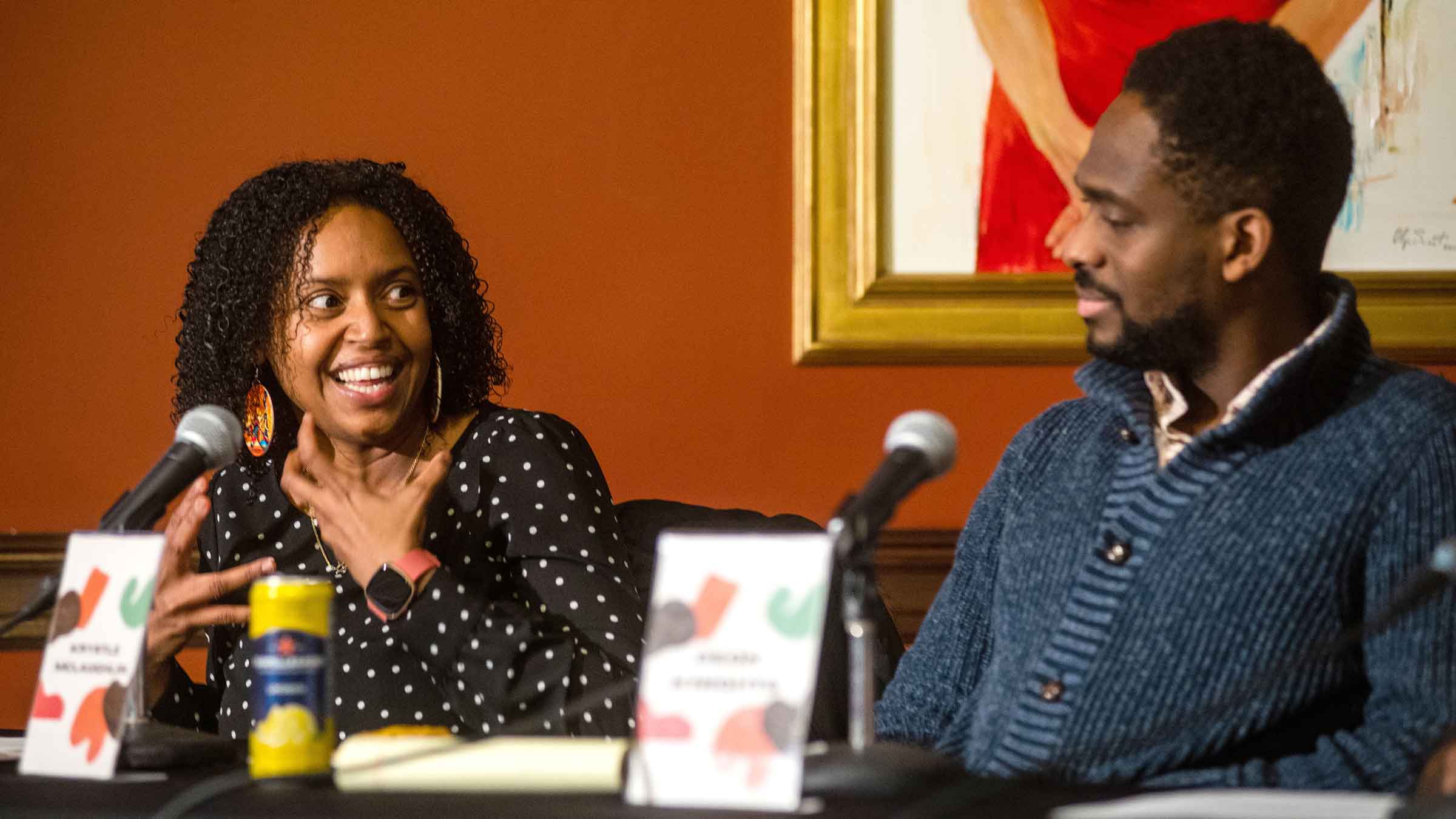 two panelists seated behind microphones, one talking and the other listening