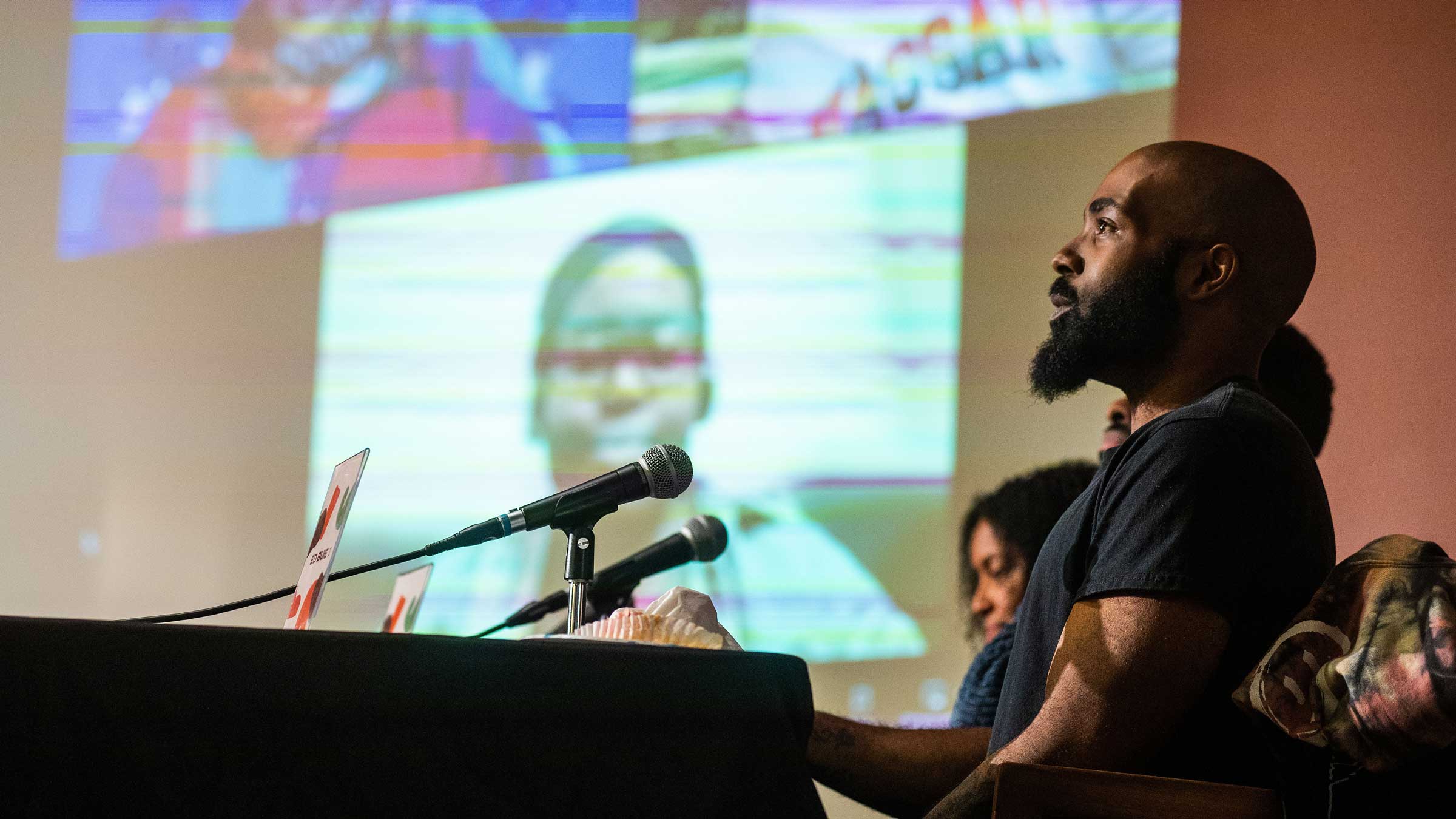 person speaking in a microphone in front of images projected on a screen