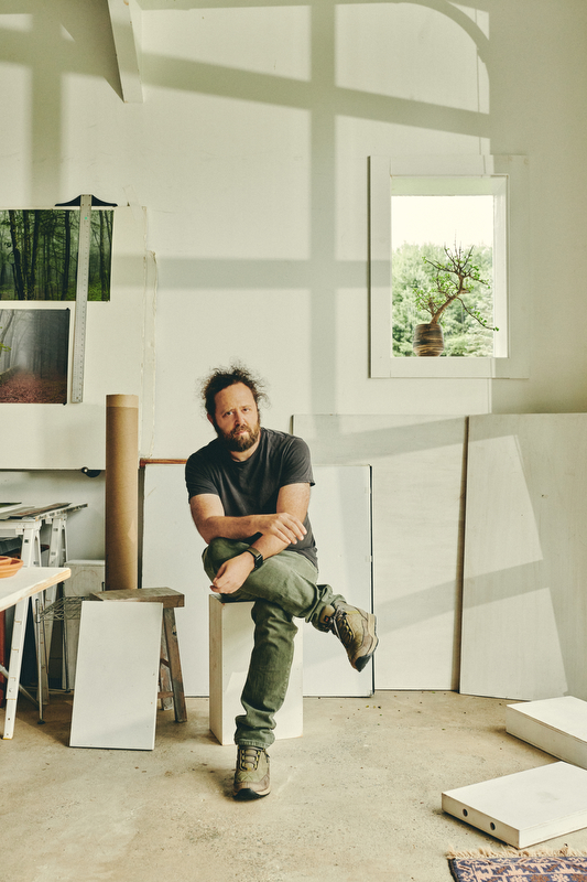 Noah Kalina seated on a stool in an art studio.