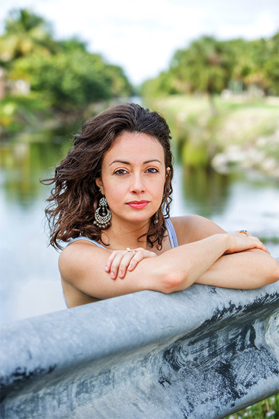 Jennine Capó Crucet leaning on a metal railing with a pond in the background.