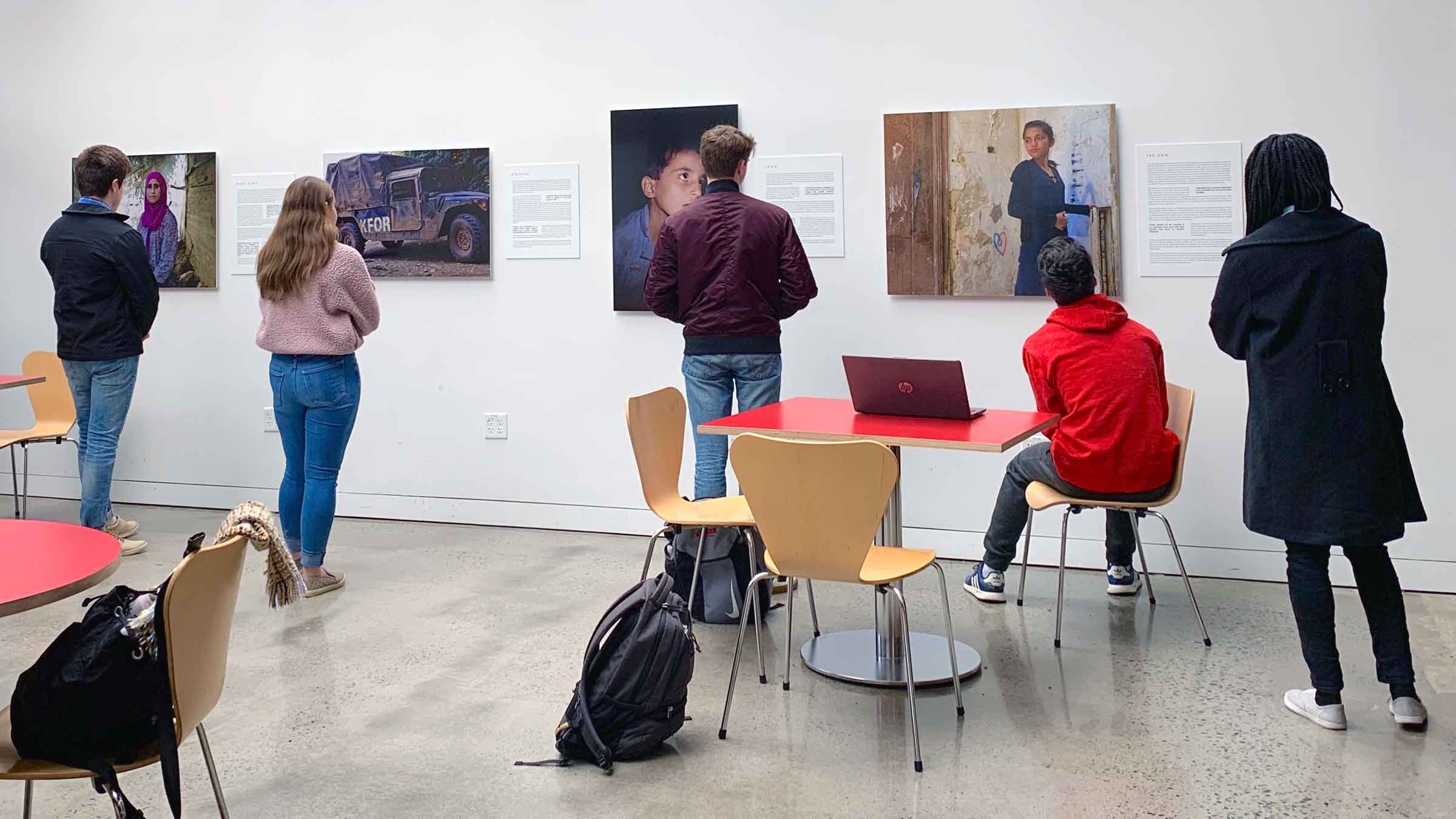 People looking at artworks on a wall with their backs facing the camera