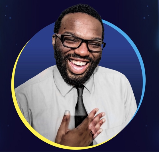 Picture of composer Shavon Lloyd; smiling wearing gray collared shirt with a black tie, hold his hand over his heart.