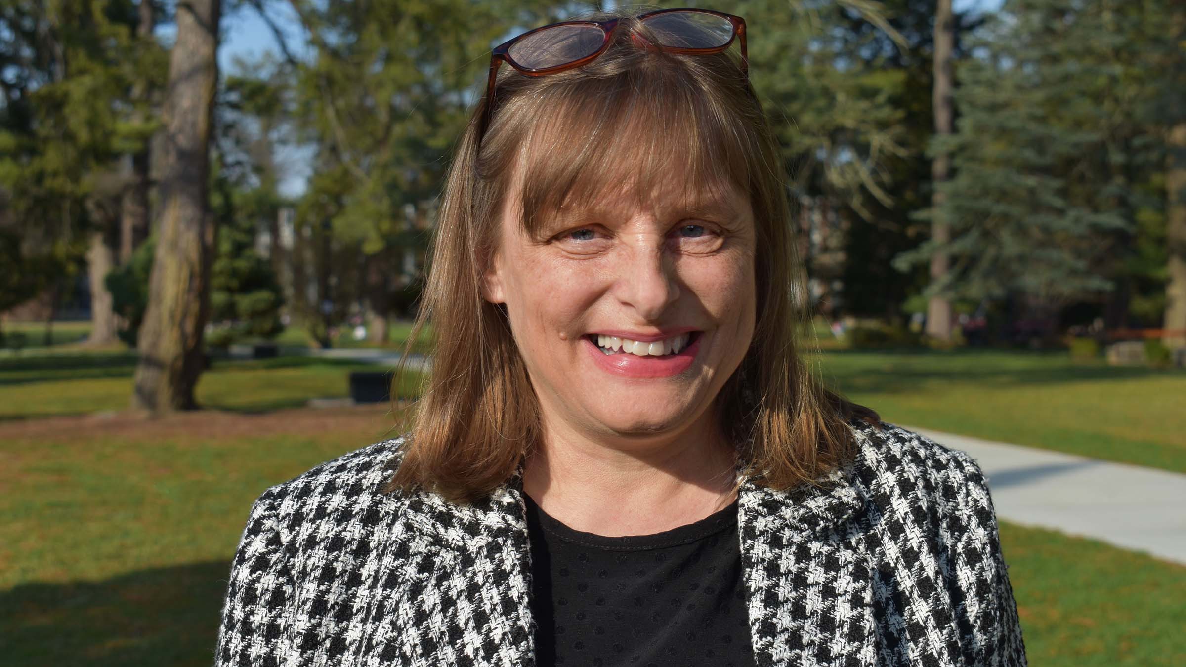 Shay Humphrey ’91, Vassar’s first general counsel wearing a black shirt and black and white jacket, standing outside with trees in the background 